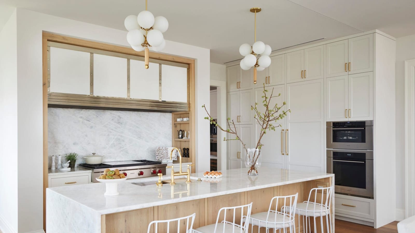 A renovated kitchen with a white quartz waterfall island, light oak cabinetry, and brass fixtures